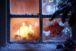 Kerstkaart: Drie witte kaarsen branden voor het raam terwijl het buiten gesneeuwd heeft