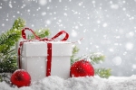 Kerstkaart: Wit kerstcadeau met een rode strik in de sneeuw met een sparrentak en twee rode kerstballen