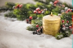 Kerstkaart: Goudkleurige brandende kaars met sparrentakken staat in de sneeuw