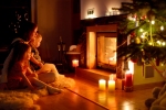 Kerstkaart: Moeder zit met twee dochters voor de open haard waar ook brandende kaarsen voor staan