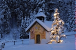 Kerstkaart: Kerstboom met brandende lichtjes naast een besneeuwde kapel