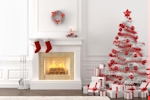 Kerstkaart: Een witte kerstboom met rode kerstversiering staat naast een witte open haard waar twee rode kerstsokken boven hangen