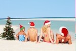 Kerstkaart: De familie zit op het strand met een kerstmuts op, er is ook een kerstboompje